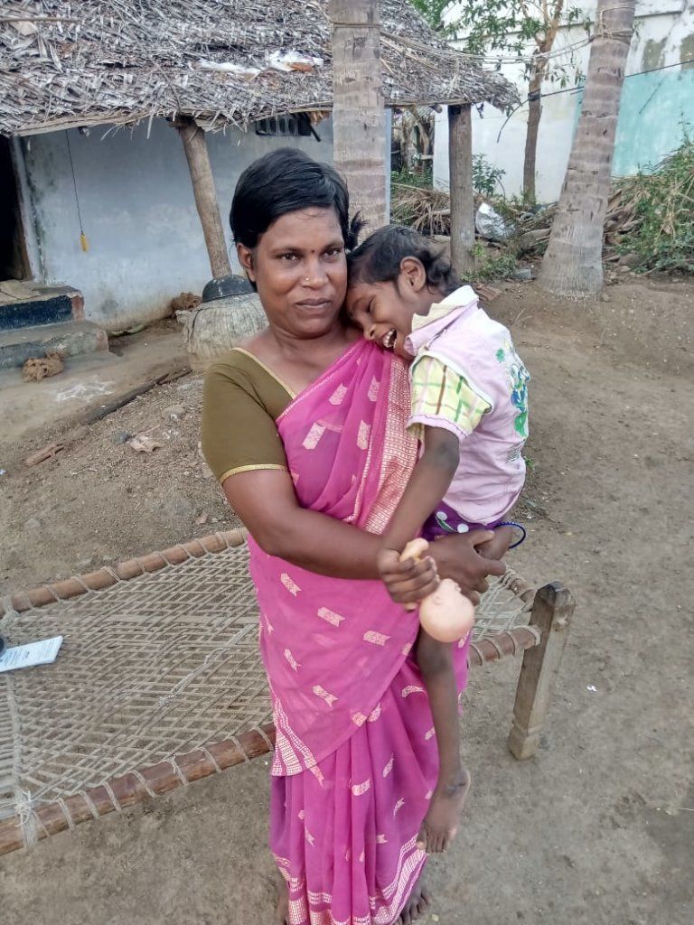 A mother holding her young child outside a village home