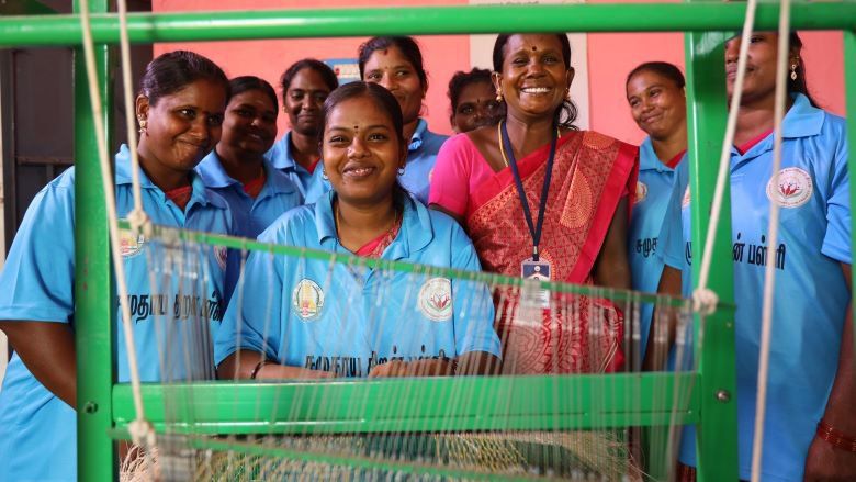 Smiling women weavers standing at a loom